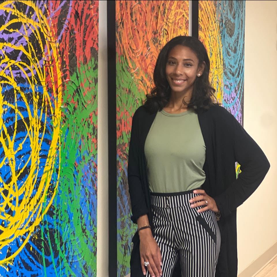 Jocelyn Van standing beside her colorful abstract paintings